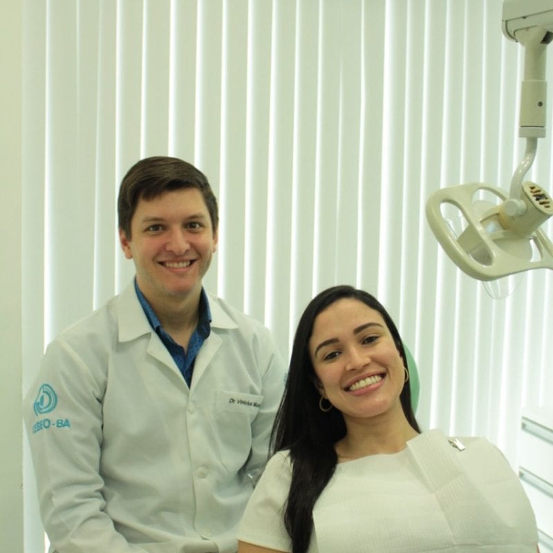 Dentista Vinícius, sentado ao lado de uma paciente em sua clínica odontológica
