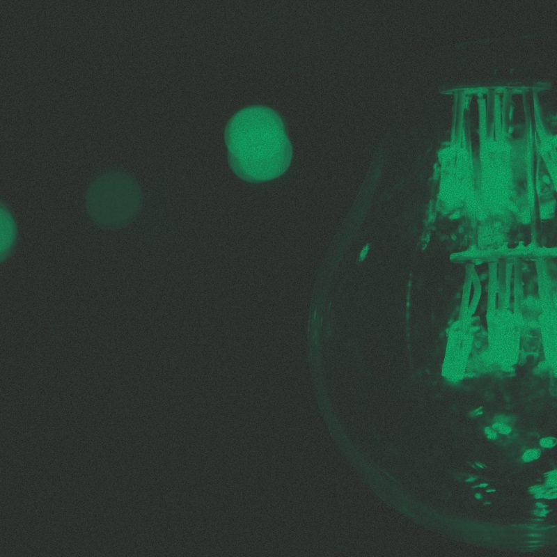 Lâmpadas acesas, uma grande em foco à direita e outras ao fundo, desfocadas. Imagem com filtro verde granulado.